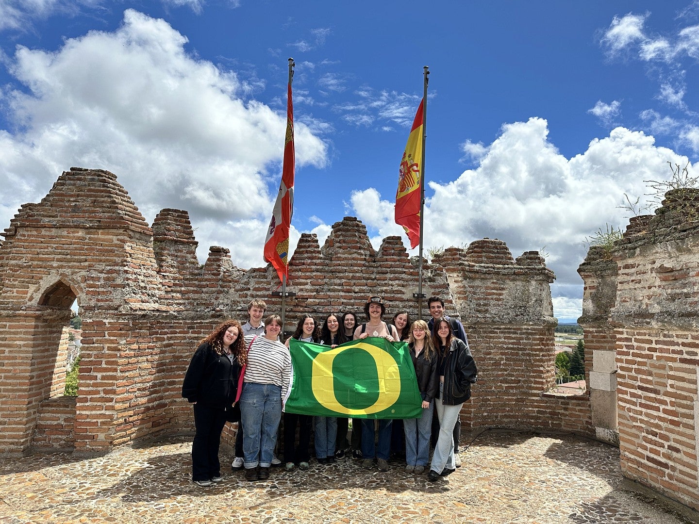 Group of college students holding a green flag with a yellow O on top of a medieval castle in Coca, Spain