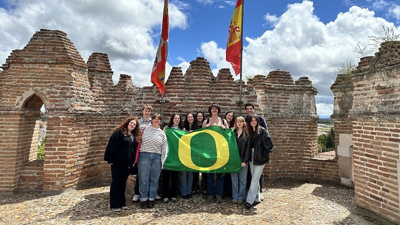 Group of college students holding a green flag with a yellow O on top of a medieval castle in Coca, Spain