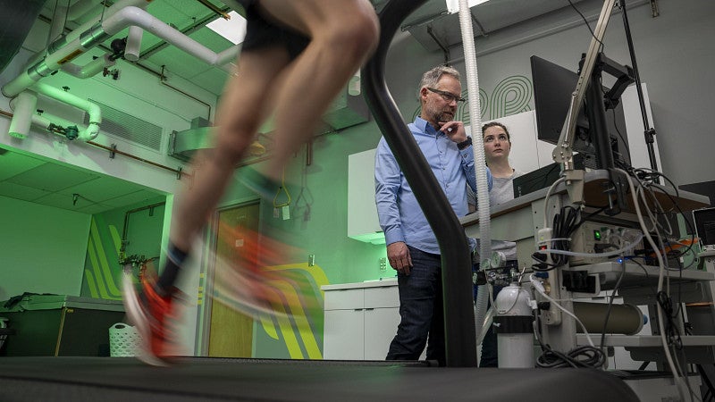 Low angle photo of an athlete running on a treadmill while being observed by two researchers