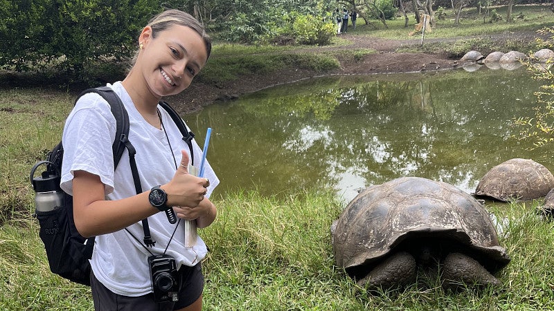College student posing with a thumbs up gesture in front of a Galapagos Giant Tortoise