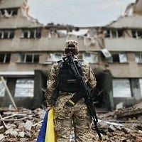 stock photo of a soldier standing in front of a destroyed building in Ukraine